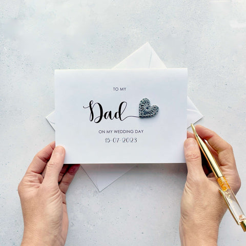 A white card with 'to my Dad on my wedding day' printed in black text. The wedding date is also on there too. The word 'Dad' is much larger than the rest of the text. There is a grey crochet heart coming off the 'd' in 'Dad'.
