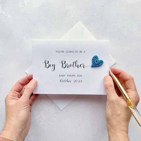 A white card with ‘You’re going to be a Big Brother’ printed on it. The words ‘Big Brother’ appears larger than the rest of the text and it has a little blue crochet heart at the end of the word.  Under the words ’Big Brother’ is the babies surname and due date making this card a lovely keepsake. 