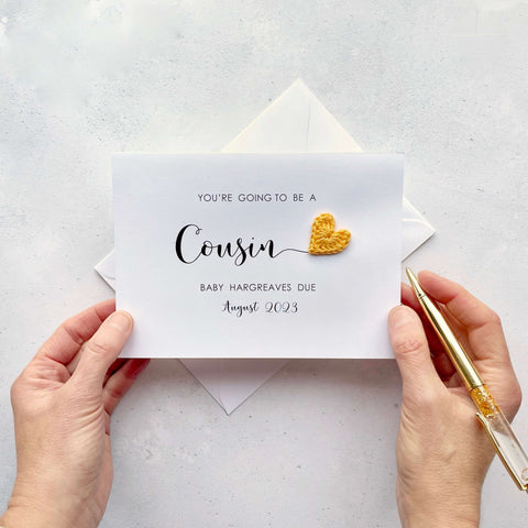 A white card with ‘You’re going to be a Cousin’ printed on it. The word ‘Cousin’ appears larger than the rest of the text and it has a little yellow crochet heart at the end of the word.  Under the word ’Cousin’ is the babies surname and due date making this card a lovely keepsake. 