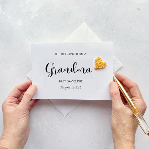 A white card with ‘You’re going to be Grandma’ printed on it. The word ‘Grandma’ appears larger than the rest of the text and it has a little yellow crochet heart at the end of the word.  Under the word ’Grandma’ is the babies surname and due date making this card a lovely keepsake. 