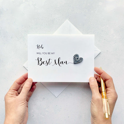 A white card with ‘Will you be my Best Man’ printed on it. The words ‘Best Man’ appears larger than the rest of the text and it has a little grey crochet heart at the end of the word.  The name ‘Rob’ has been printed at the top of the text, making this card a lovely keepsake. 