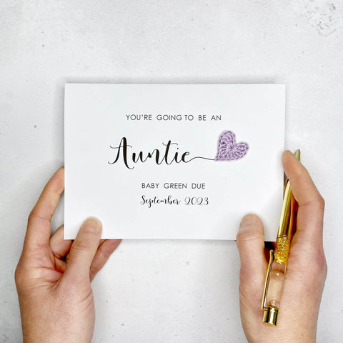 A white card with ‘You’re going to be an Auntie’ printed on it. The word ‘Auntie’ appears larger than the rest of the text and it has a little lilac crochet heart at the end of the word.  Under the word ’Auntie’ is the babies surname and due date making this card a lovely keepsake. 