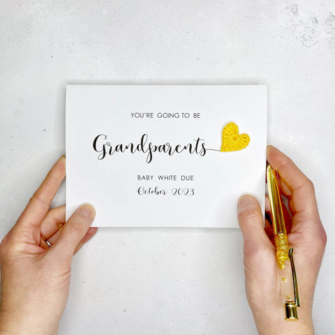 A white card with ‘You’re going to be Grandparents’ printed on it. The word “Grandparents appears larger than the rest of the text and it has a little yellow crochet heart at the end of the word.  Under the word “grandparents’ is the babies surname and due date making this card a lovely keepsake. 