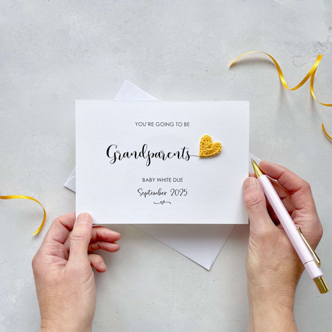 A landscape pregnancy announcement card with the text “You’re going to be Grandparents” in elegant black font. Below, it says “Baby White due September 2025,” with a small decorative flourish. The card features a small crocheted yellow heart.