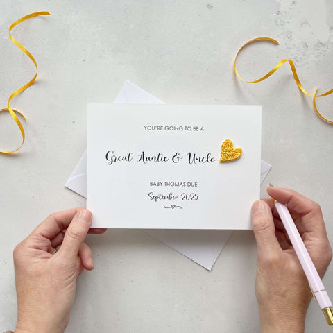 A landscape pregnancy announcement card with the text “You’re going to be a Great Auntie & Uncle” in elegant black font. Below, it says “Baby Thomas due September 2025,” with a small decorative flourish. The card features a small crocheted yellow heart.