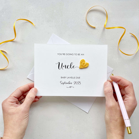 A landscape pregnancy announcement card with the text “You’re going to be an Uncle” in elegant black font. Below, it says “Baby Lavelle due September 2025,” with a small decorative flourish. The card features a small crocheted yellow heart.